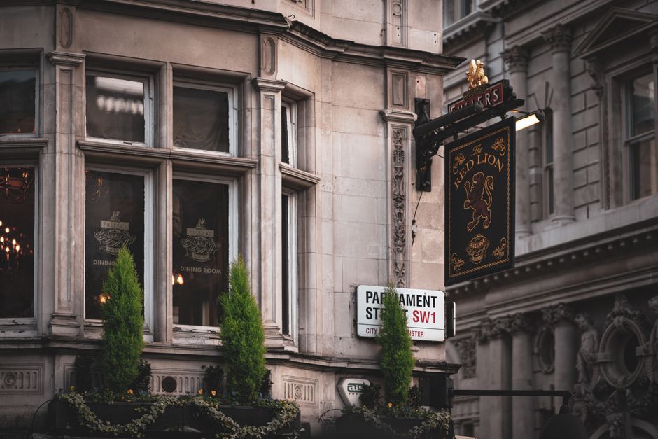 A close-up view of the exterior of The Red Lion pub situated on Red Lion Square in Holborn, WC1. The building features ornate stone architecture with large, multi-pane windows, each divided by decorat